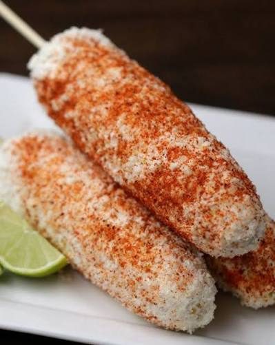 Two elotes dusted with chili and cheese, with a lime wedge