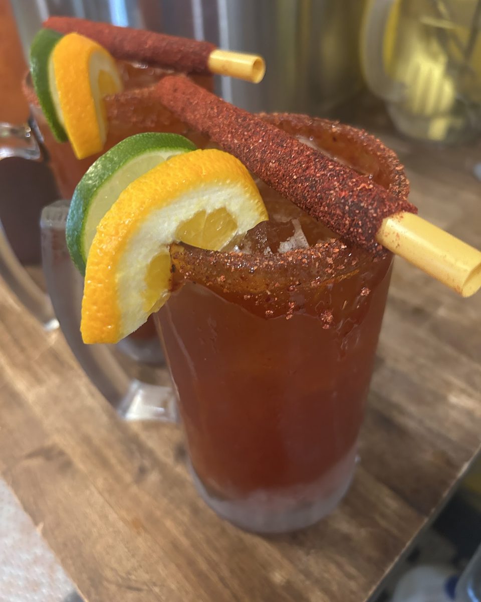 A michelada rimmed with chili powder, with an orange slice and a tamarind candy stick